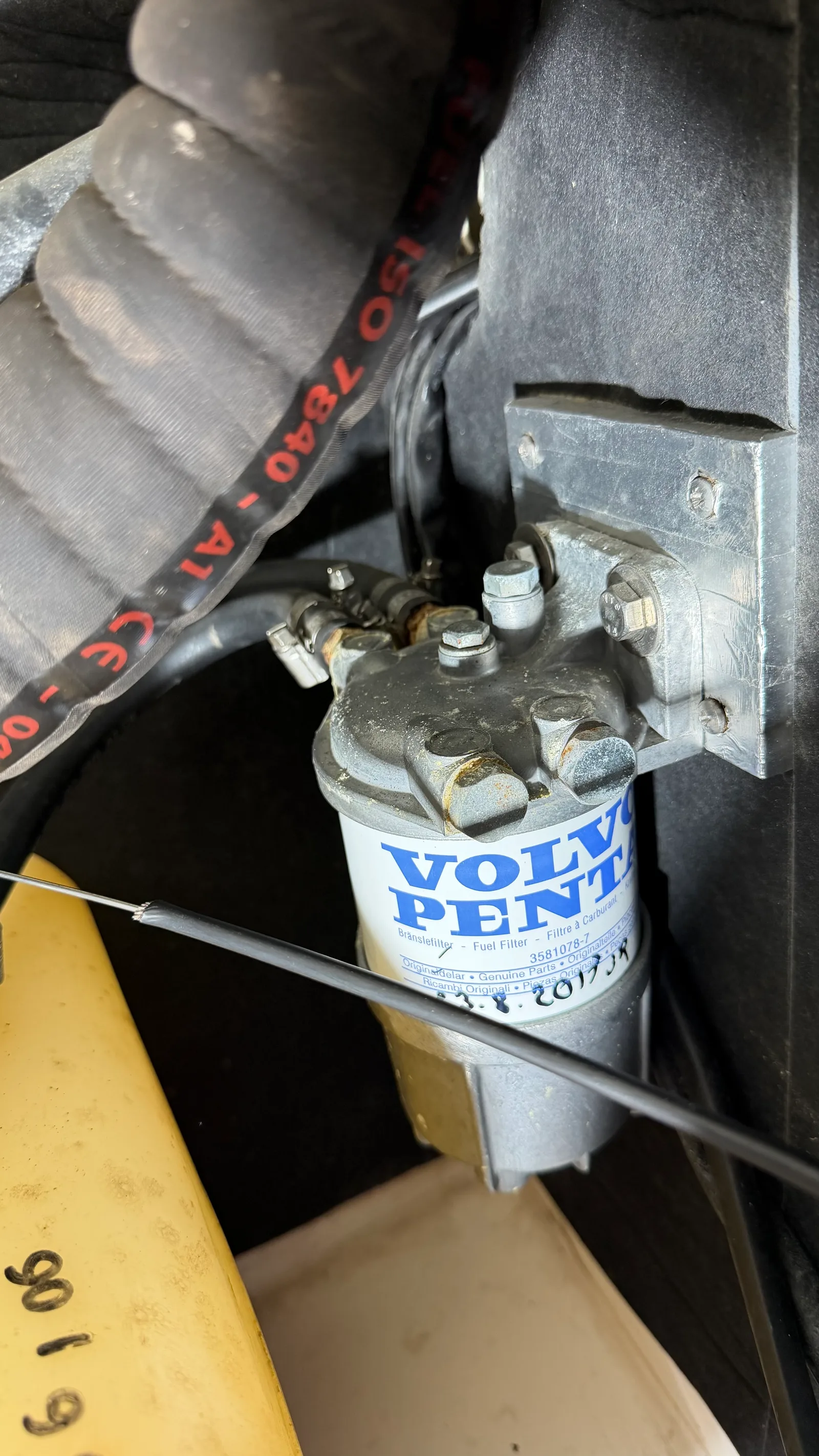 Ancienne installation avant refit : bloc pré-filtre monté sur cloison avec filtre spin-on Volvo Penta d'origine daté 2019, durite de gasoil marine noire au marquage ISO 7840 A1 apparent