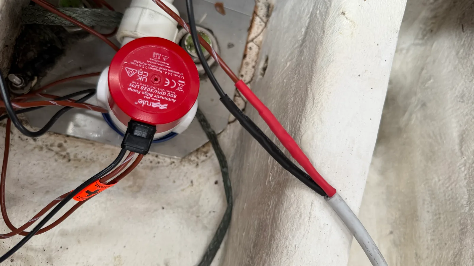 Pompe de cale automatique Rule 800 Auto 205A installée en fond de cale sur JAMAIS : détecteur de niveau intégré, fils positif et négatif protégés par gaine thermorétractable rouge et noire