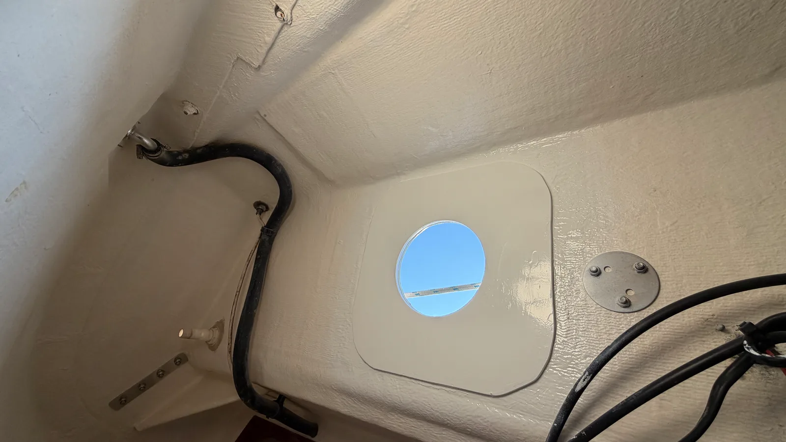 Passe-coque hors-bord du refoulement de la pompe manuelle, vu de l'intérieur : ciel visible à travers la sortie, base FP4 blanche finalisée et scellée