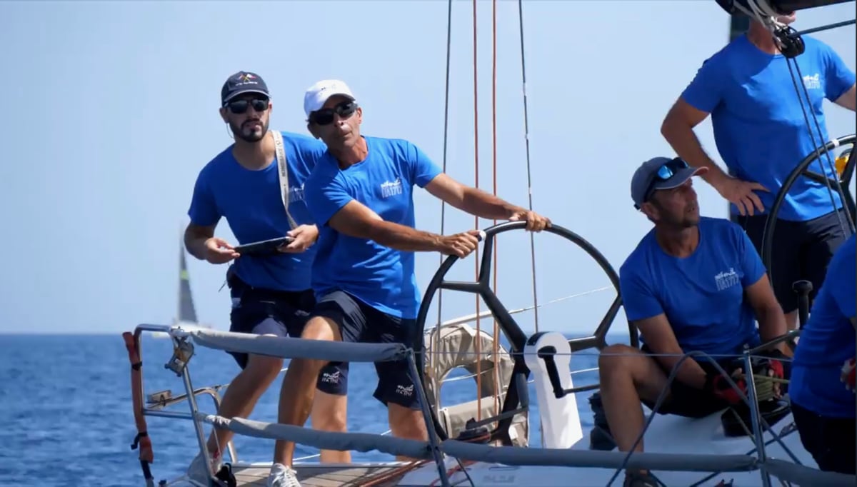 Enrico Bruschini en casquette bleue, navigateur, transmet une décision tactique à l'oreille du barreur pendant une régate en Méditerranée.