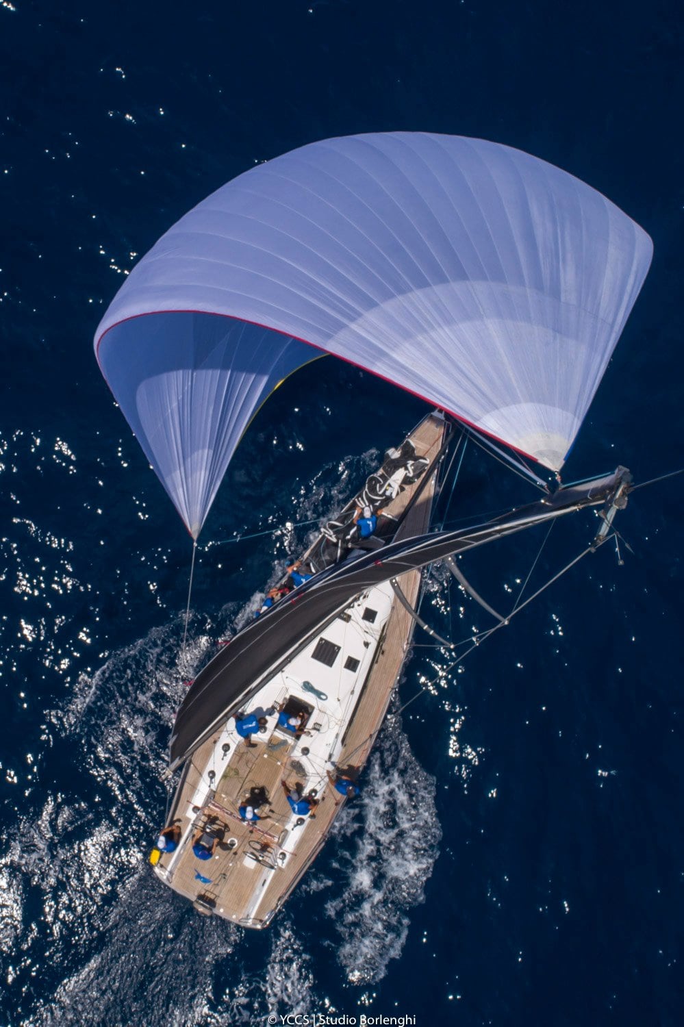 Vue aérienne d'un voilier de régate sous spinnaker en pleine course, équipage à bord en pleine action.